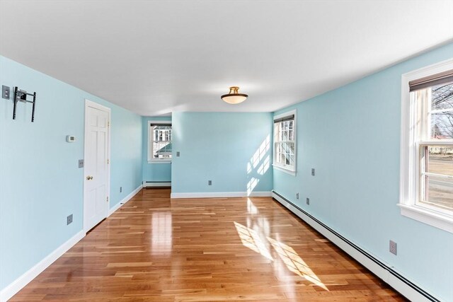 spare room featuring a baseboard heating unit, baseboards, light wood-type flooring, and baseboard heating