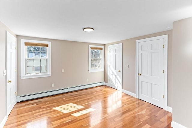 unfurnished bedroom featuring a baseboard heating unit, baseboards, and light wood-type flooring