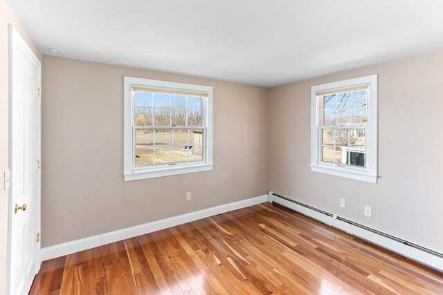 empty room with a baseboard heating unit, baseboards, and hardwood / wood-style floors