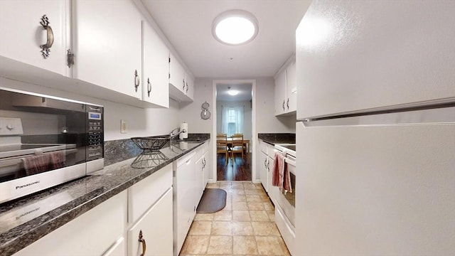 kitchen with white appliances, white cabinets, a sink, and dark stone counters