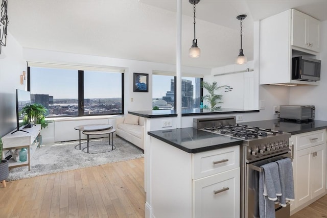 kitchen with stainless steel gas range oven, dark countertops, white cabinets, and light wood-style floors