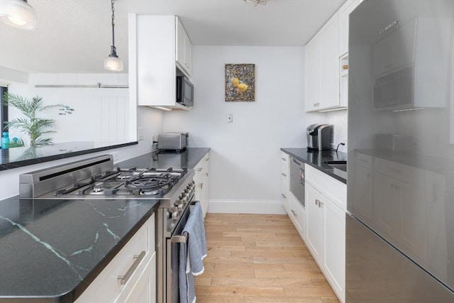 kitchen with gas stove, black microwave, baseboards, light wood finished floors, and white cabinetry