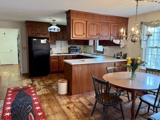 kitchen featuring light countertops, a chandelier, freestanding refrigerator, a peninsula, and stainless steel microwave