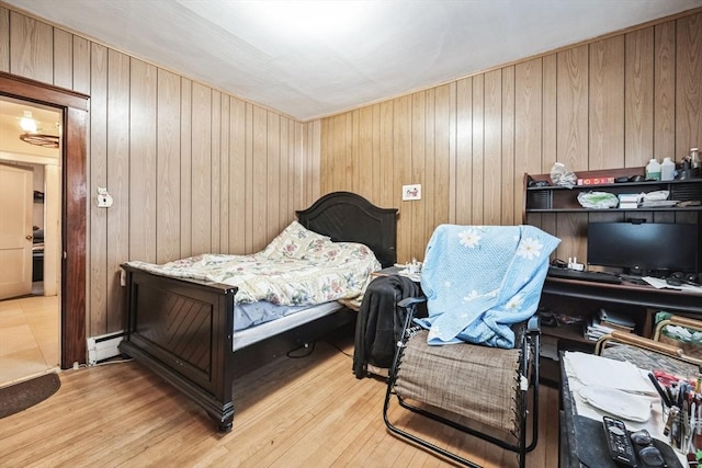 bedroom featuring baseboard heating, wooden walls, and light wood-type flooring