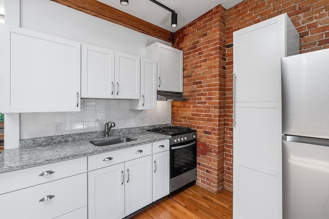 31 Division St # 3, Chelsea, MA 02150 - kitchen featuring appliances with stainless steel finishes, under cabinet range hood, brick wall, light wood-style floors, and white cabinetry