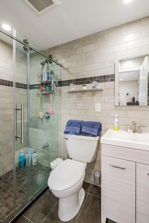 2171 Commonwealth Ave, Newton, MA 02466 - bathroom featuring tile patterned flooring, toilet, vanity, a stall shower, and tile walls