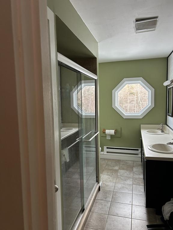 bathroom featuring a baseboard heating unit, a stall shower, tile patterned flooring, and a sink