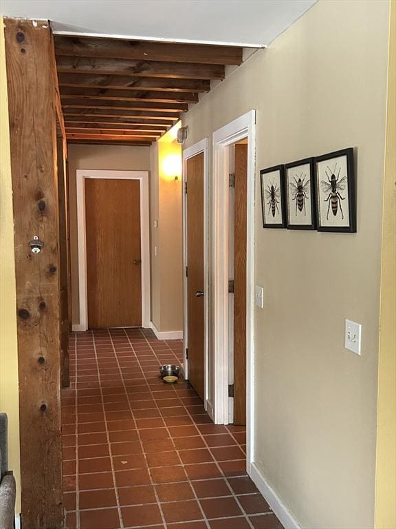 hall featuring beamed ceiling and baseboards