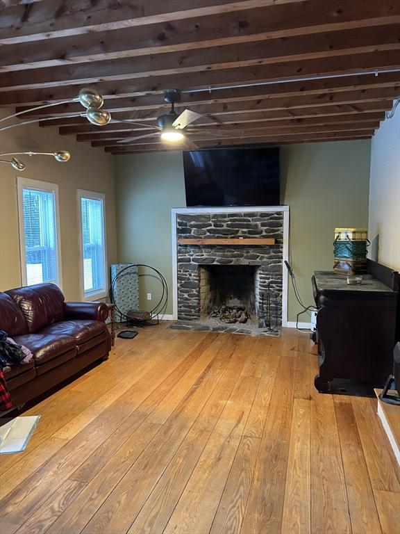 living area with baseboards, ceiling fan, beam ceiling, a fireplace, and hardwood / wood-style flooring