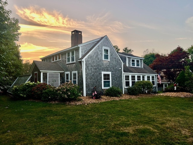 back house at dusk featuring a lawn