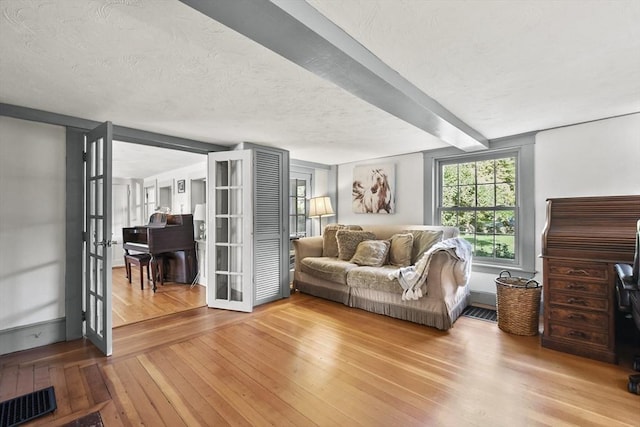 living area featuring visible vents, beam ceiling, french doors, a textured ceiling, and wood-type flooring