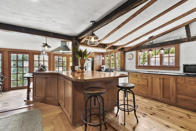 kitchen with brown cabinets, lofted ceiling with beams, a breakfast bar area, wall chimney range hood, and dishwasher