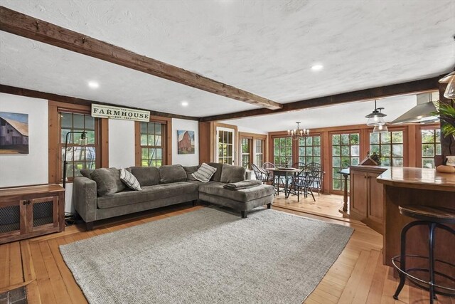 living area featuring light wood-type flooring, beam ceiling, a textured ceiling, and an inviting chandelier