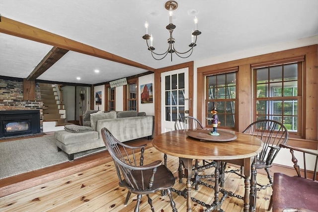 dining area featuring beamed ceiling, a fireplace with flush hearth, wood-type flooring, and a chandelier