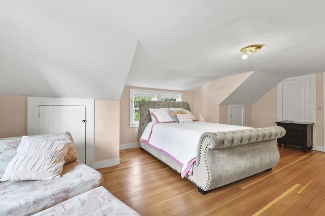 bedroom with vaulted ceiling, baseboards, and light wood finished floors