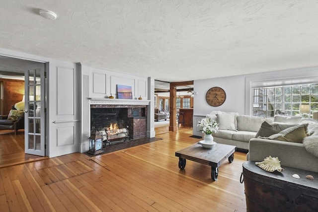 living area featuring a fireplace with flush hearth, light wood-style flooring, and a textured ceiling