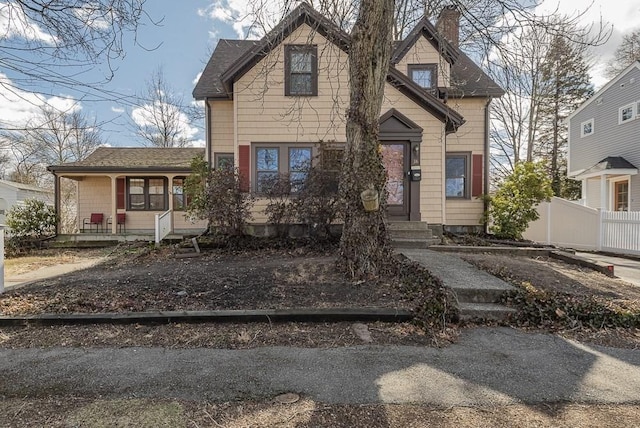 view of front of home featuring covered porch, a shingled roof, a chimney, and fence