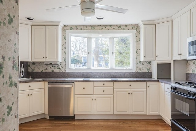 kitchen with dark countertops, wallpapered walls, stainless steel appliances, and a sink