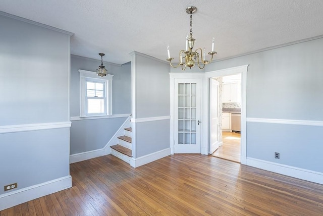 unfurnished dining area with a textured ceiling, hardwood / wood-style flooring, a notable chandelier, baseboards, and stairway