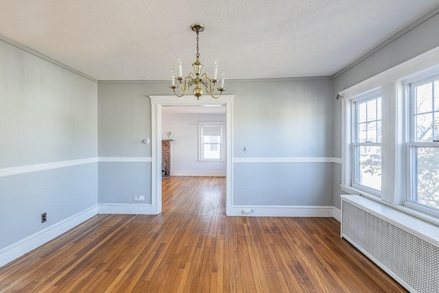 empty room featuring baseboards, radiator heating unit, ornamental molding, hardwood / wood-style floors, and a notable chandelier