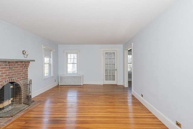 unfurnished living room with baseboards, radiator heating unit, light wood-type flooring, and a brick fireplace