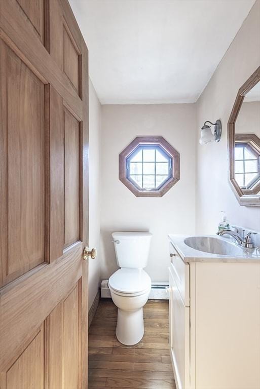 bathroom featuring vanity, baseboard heating, wood finished floors, and toilet