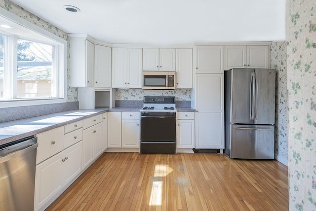 kitchen with stainless steel appliances, light countertops, white cabinets, and wallpapered walls