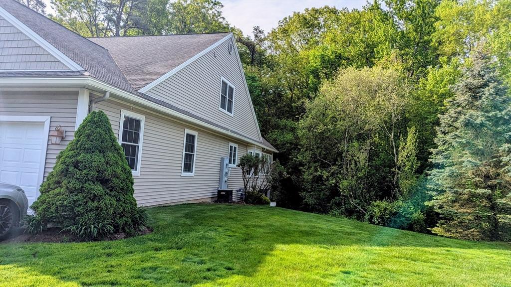 view of side of home featuring a yard, a garage, and a shingled roof