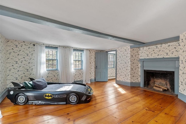 bedroom featuring hardwood / wood-style floors, baseboards, wallpapered walls, a fireplace with flush hearth, and beamed ceiling