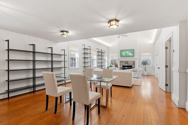 dining space featuring lofted ceiling, a glass covered fireplace, light wood-style floors, baseboards, and ceiling fan