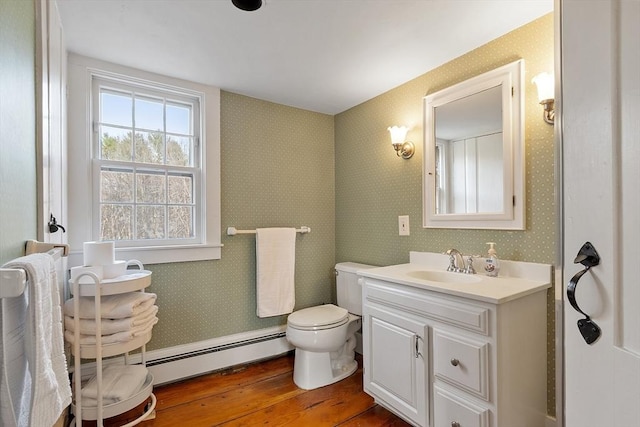 bathroom featuring toilet, a baseboard heating unit, wood finished floors, wallpapered walls, and vanity