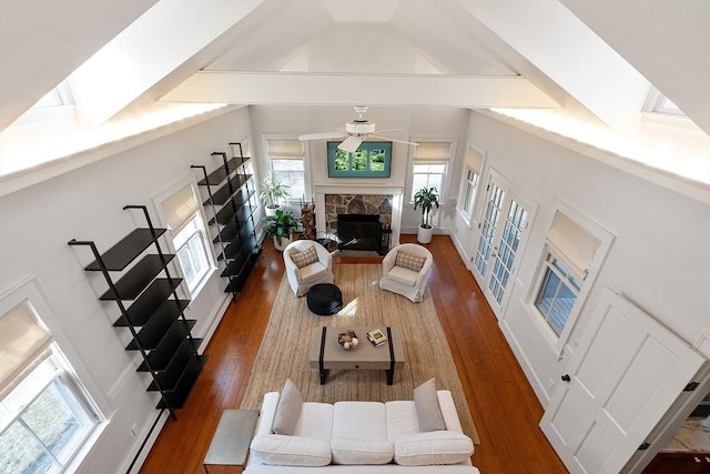 living area featuring a stone fireplace, wood finished floors, baseboard heating, and ceiling fan