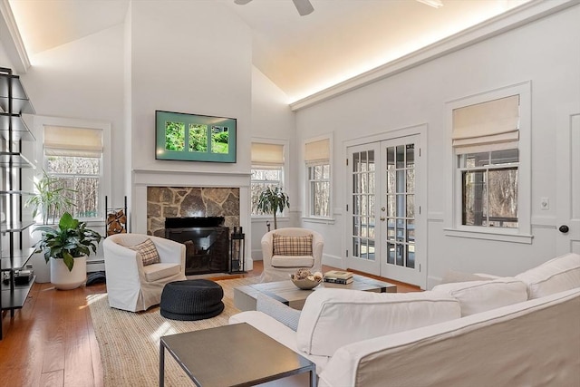 living room featuring a wealth of natural light, a stone fireplace, french doors, and wood finished floors