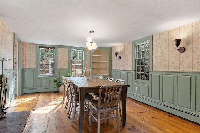 dining room featuring baseboard heating, wainscoting, wallpapered walls, and light wood-style flooring