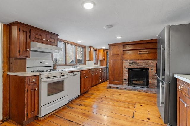 kitchen featuring a brick fireplace, under cabinet range hood, light wood-type flooring, light countertops, and white appliances