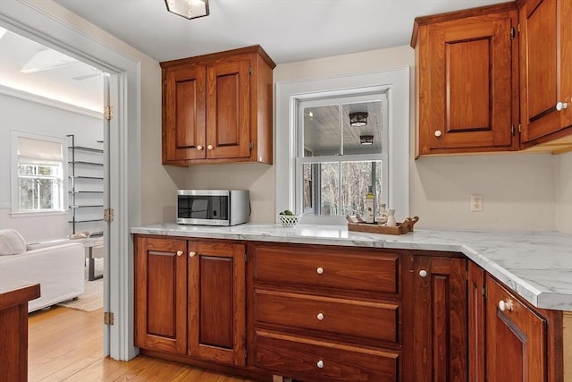 kitchen featuring brown cabinetry, stainless steel microwave, and light wood-type flooring