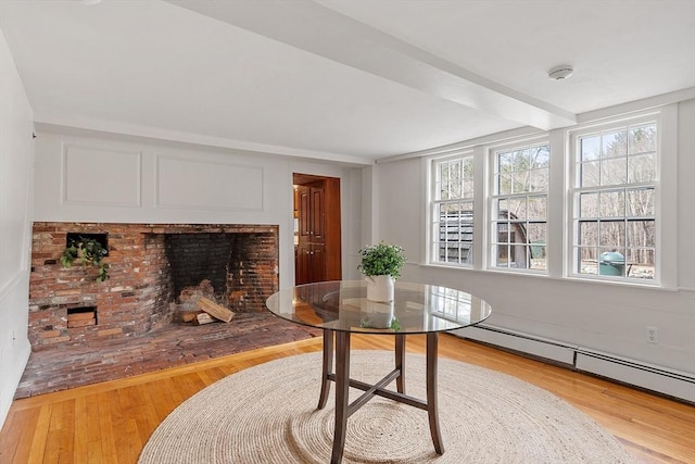 dining room with a baseboard radiator, beamed ceiling, light wood-style flooring, and a fireplace