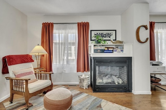 sitting room with a glass covered fireplace, baseboards, wood finished floors, and visible vents