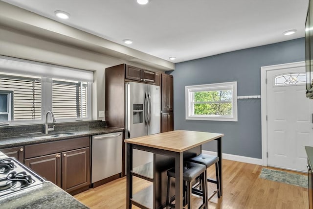 kitchen with dark brown cabinetry, baseboards, light wood-type flooring, a sink, and appliances with stainless steel finishes