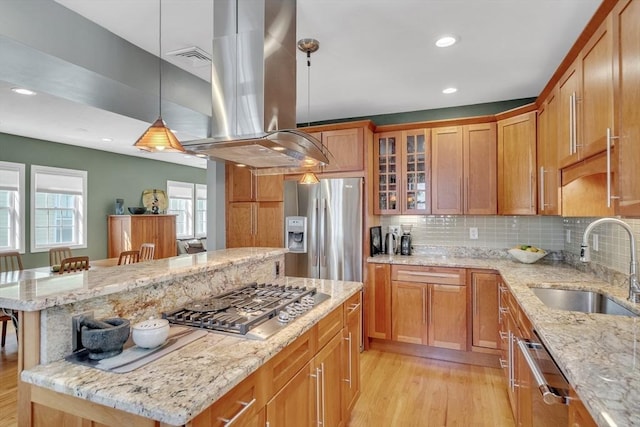 kitchen with island range hood, appliances with stainless steel finishes, tasteful backsplash, a sink, and light wood finished floors