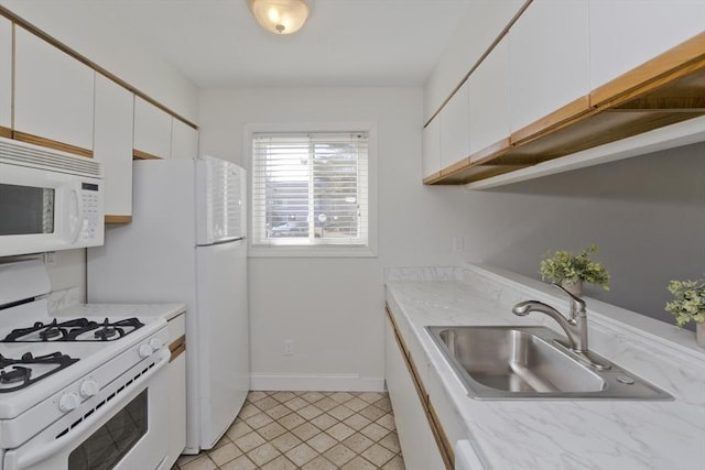 kitchen featuring white appliances, white cabinets, a sink, and baseboards