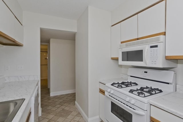 kitchen with a sink, white appliances, white cabinets, and light countertops