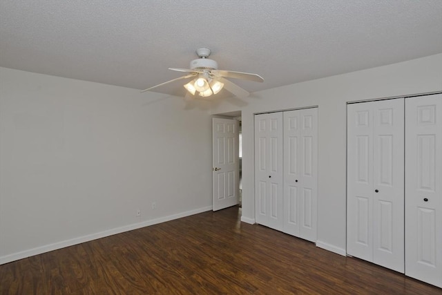 unfurnished bedroom featuring a textured ceiling, baseboards, dark wood-type flooring, and multiple closets