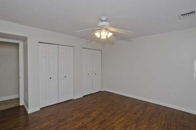 unfurnished bedroom featuring dark wood-style floors, multiple closets, visible vents, a textured ceiling, and baseboards