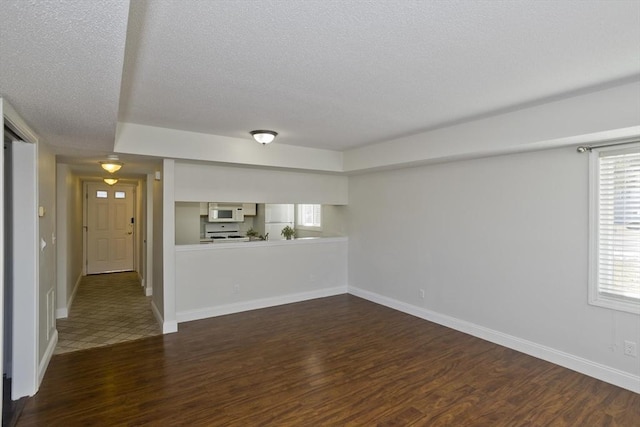 empty room with dark wood-style flooring, a textured ceiling, and baseboards