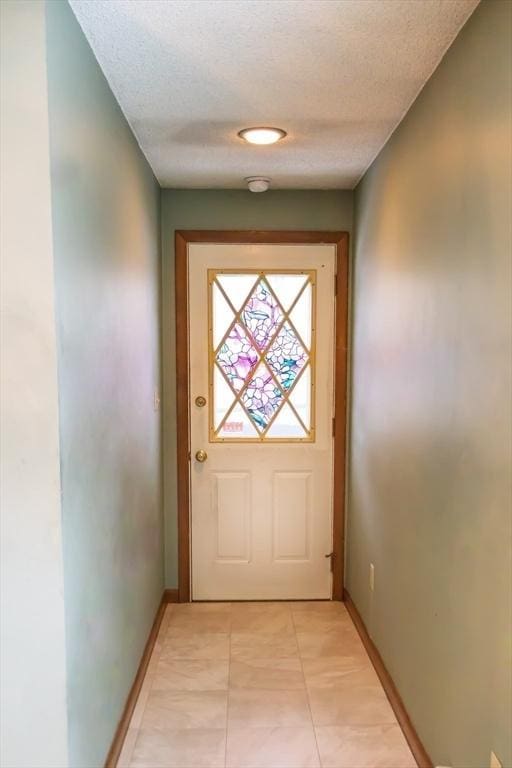 doorway to outside featuring baseboards, a textured ceiling, and light tile patterned flooring