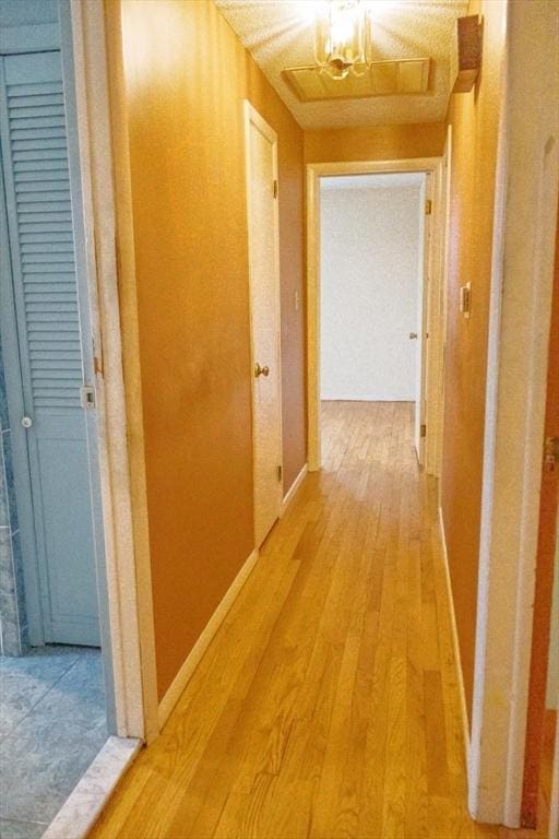 hall with light wood-style flooring, a chandelier, and baseboards