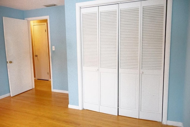 unfurnished bedroom featuring light wood finished floors, baseboards, and a closet