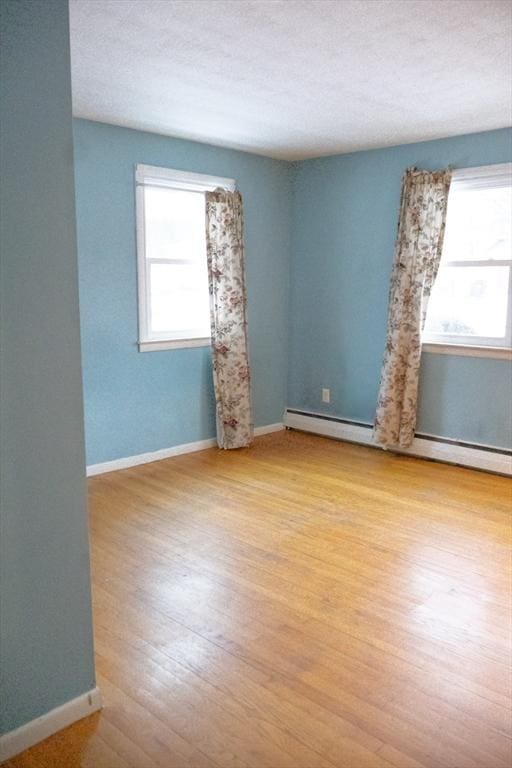 empty room featuring a textured ceiling, baseboards, baseboard heating, and wood finished floors