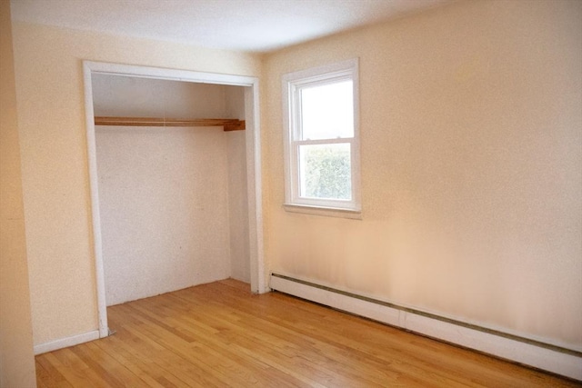 unfurnished bedroom featuring a closet, baseboard heating, and wood finished floors